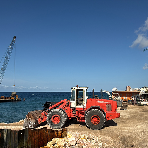 Rode shovel aan het werk op een kustbouwlocatie met kraan en helderblauwe zee op de achtergrond