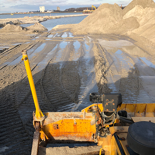 Zandverzet met bulldozer op een bouwterrein aan het water met stapels zand en sporen in de modder