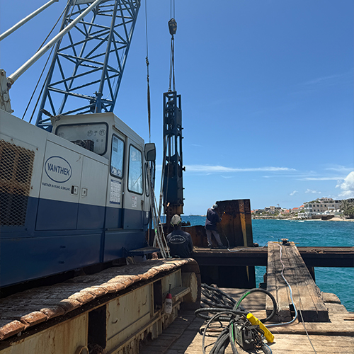 Heistelling en bouwpersoneel aan het werk op een houten werkplatform bij een kustproject met helderblauw water